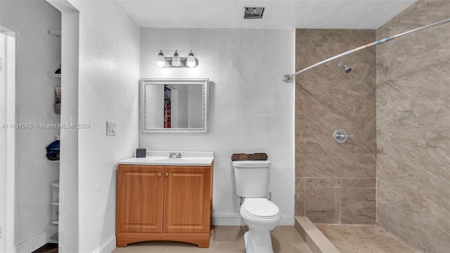 bathroom featuring tile patterned flooring, a tile shower, vanity, and toilet