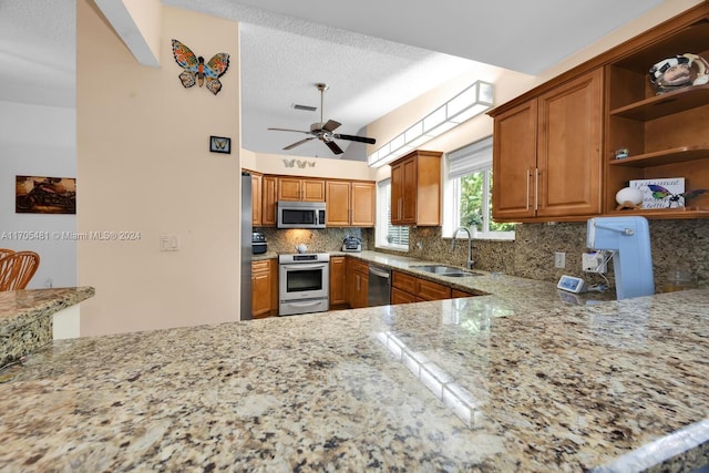 kitchen with sink, ceiling fan, appliances with stainless steel finishes, light stone counters, and kitchen peninsula