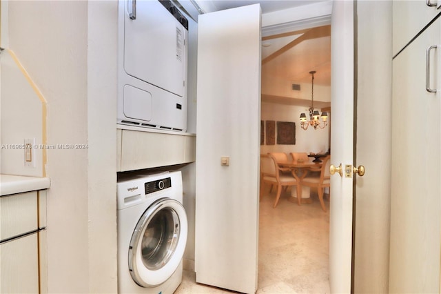 clothes washing area with stacked washer and clothes dryer and an inviting chandelier