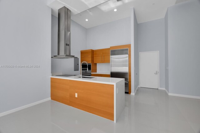 kitchen with kitchen peninsula, stainless steel built in refrigerator, black electric cooktop, sink, and wall chimney range hood