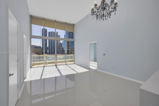 empty room featuring floor to ceiling windows, tile patterned flooring, a towering ceiling, and an inviting chandelier