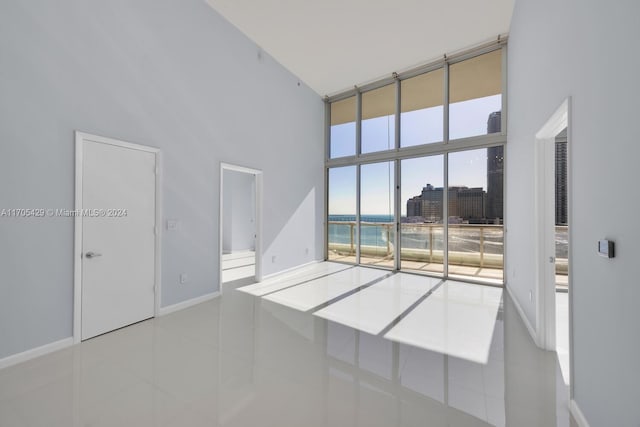 unfurnished room featuring a water view, light tile patterned floors, and a high ceiling