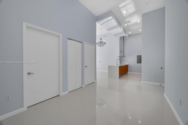 tiled empty room with a chandelier, a towering ceiling, and sink