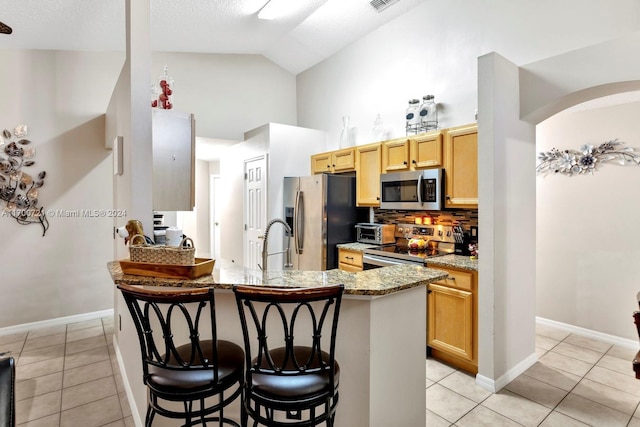 kitchen featuring stainless steel appliances, light stone counters, a breakfast bar area, light brown cabinetry, and light tile patterned floors