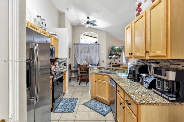 kitchen with appliances with stainless steel finishes, light stone counters, vaulted ceiling, sink, and light tile patterned floors