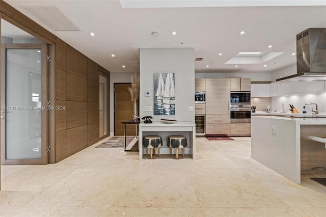 kitchen with stainless steel appliances, wall chimney range hood, white cabinetry, a kitchen island, and a breakfast bar area