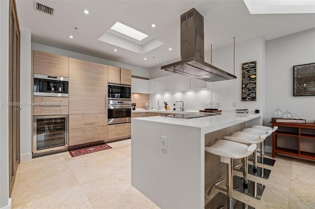 kitchen with stainless steel appliances, kitchen peninsula, island range hood, a breakfast bar, and white cabinets