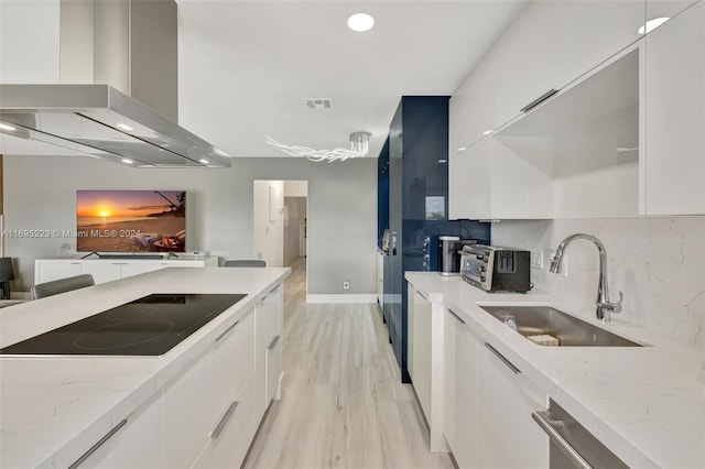 kitchen with white cabinetry, sink, wall chimney range hood, light stone counters, and light hardwood / wood-style floors