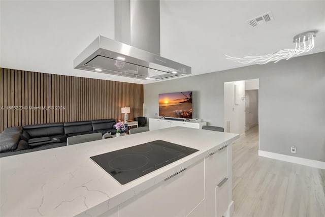 kitchen featuring white cabinetry, light stone countertops, wall chimney range hood, black electric stovetop, and light wood-type flooring