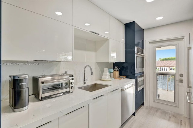 kitchen with light stone countertops, stainless steel appliances, sink, light hardwood / wood-style floors, and white cabinetry