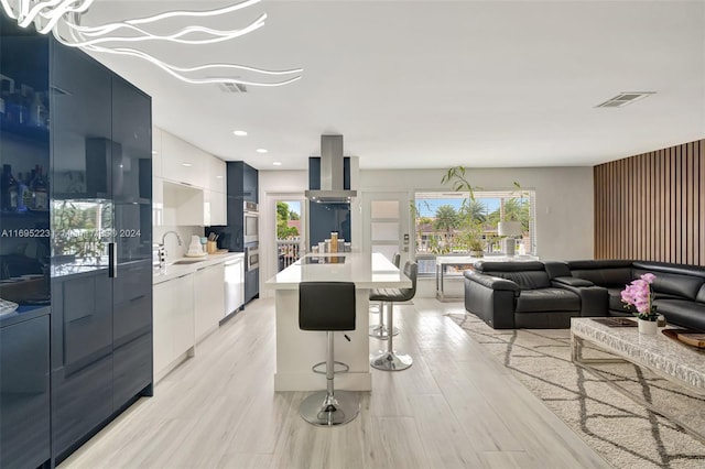 kitchen featuring white cabinetry, wall chimney range hood, light hardwood / wood-style floors, a kitchen bar, and a kitchen island