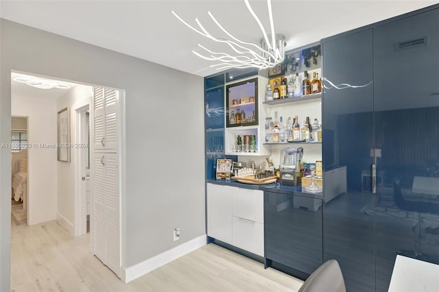 bar with light wood-type flooring, blue cabinets, and a notable chandelier