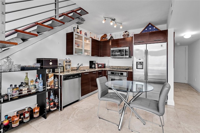 kitchen with dark brown cabinets, stainless steel appliances, light stone counters, and sink