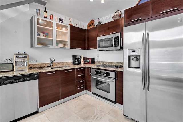 kitchen with sink, a textured ceiling, appliances with stainless steel finishes, light stone counters, and dark brown cabinetry