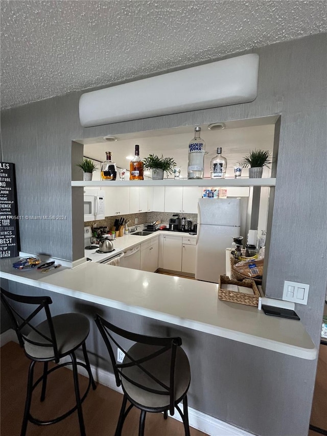 kitchen with kitchen peninsula, a kitchen breakfast bar, white appliances, sink, and white cabinetry