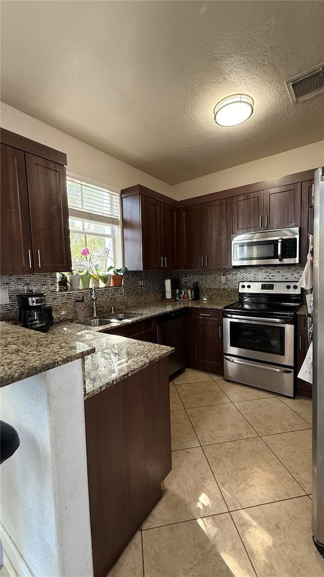 kitchen featuring stainless steel appliances, backsplash, dark stone countertops, a textured ceiling, and light tile patterned floors