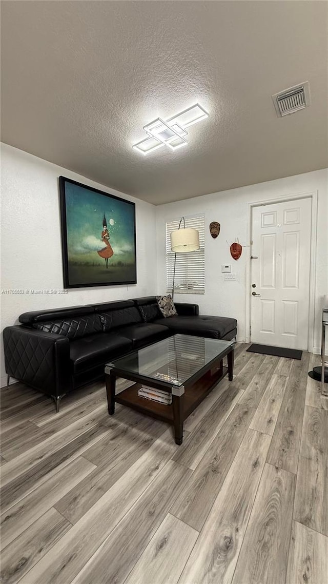 living area featuring a textured ceiling, light wood finished floors, and visible vents