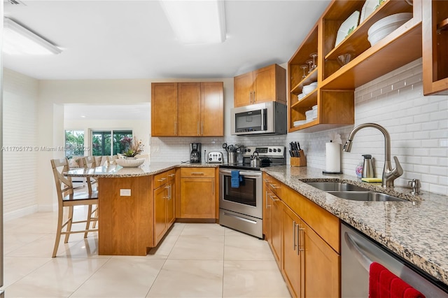 kitchen featuring a sink, a peninsula, brown cabinets, and stainless steel appliances