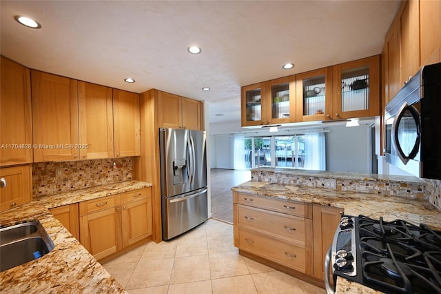 kitchen with light tile patterned floors, sink, appliances with stainless steel finishes, light stone counters, and kitchen peninsula