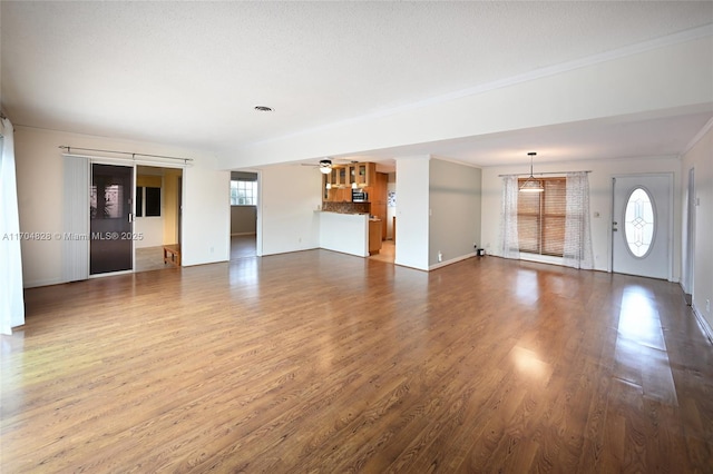 unfurnished living room featuring hardwood / wood-style floors, crown molding, a healthy amount of sunlight, and ceiling fan