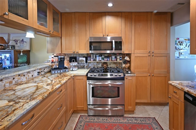 kitchen with tasteful backsplash, light stone counters, light tile patterned floors, and appliances with stainless steel finishes