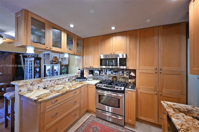 kitchen with kitchen peninsula, light stone counters, ceiling fan, and stainless steel appliances