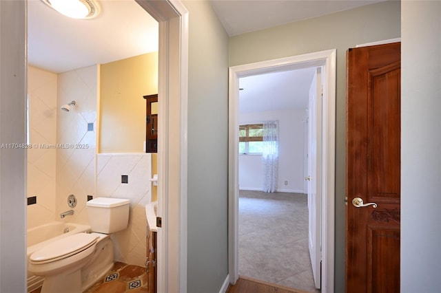 bathroom with tiled shower / bath combo, tile walls, and toilet