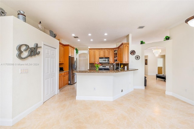 kitchen with appliances with stainless steel finishes, dark stone countertops, decorative backsplash, kitchen peninsula, and light tile patterned floors