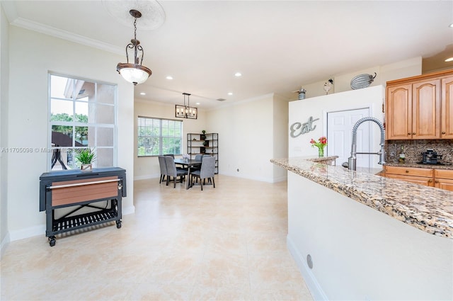 kitchen with light stone countertops, pendant lighting, decorative backsplash, sink, and ornamental molding