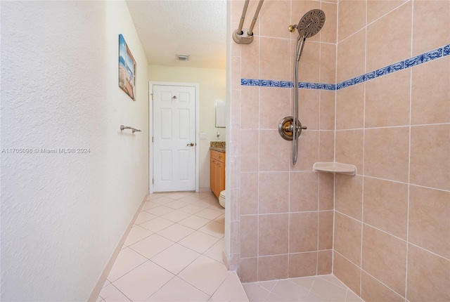 bathroom featuring toilet, vanity, a tile shower, and tile patterned flooring