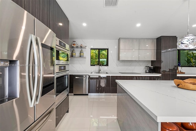 kitchen featuring sink, hanging light fixtures, stainless steel appliances, light stone counters, and light tile patterned floors