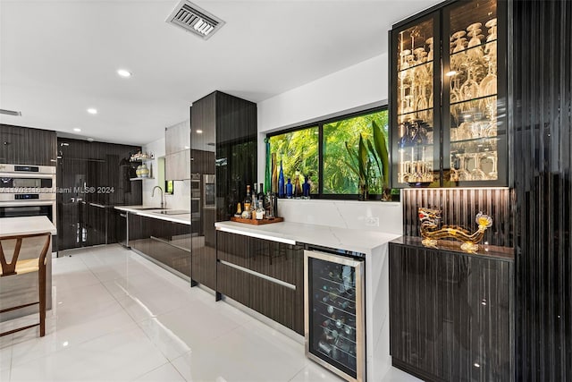 interior space with sink, stainless steel double oven, beverage cooler, light stone counters, and light tile patterned flooring