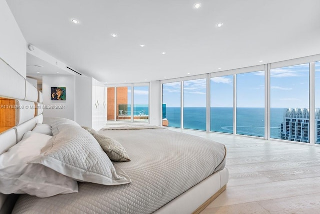 bedroom featuring expansive windows, access to exterior, light wood-type flooring, and a water view