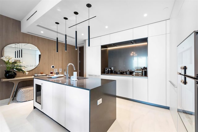 kitchen featuring sink, hanging light fixtures, white refrigerator, a center island with sink, and white cabinets