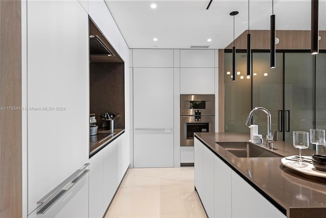 kitchen featuring pendant lighting, dark stone counters, sink, stainless steel double oven, and white cabinetry