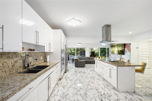 kitchen with light stone counters, island range hood, sink, and white cabinets