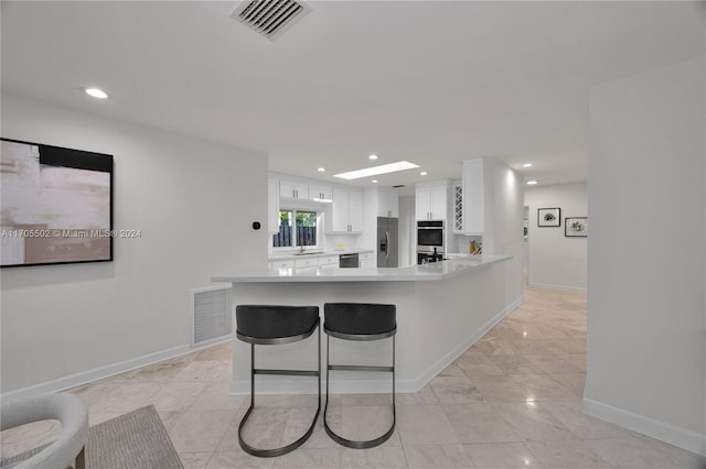 kitchen with kitchen peninsula, a kitchen breakfast bar, stainless steel appliances, sink, and white cabinetry