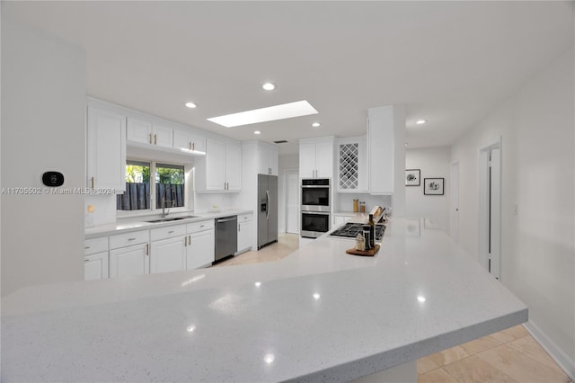 kitchen featuring a skylight, sink, kitchen peninsula, white cabinets, and appliances with stainless steel finishes