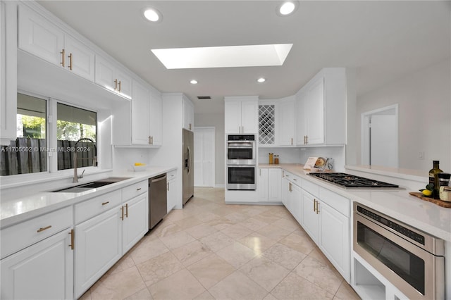 kitchen with stainless steel appliances, white cabinetry, a skylight, and sink