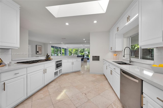 kitchen with stainless steel appliances, white cabinetry, a skylight, and sink