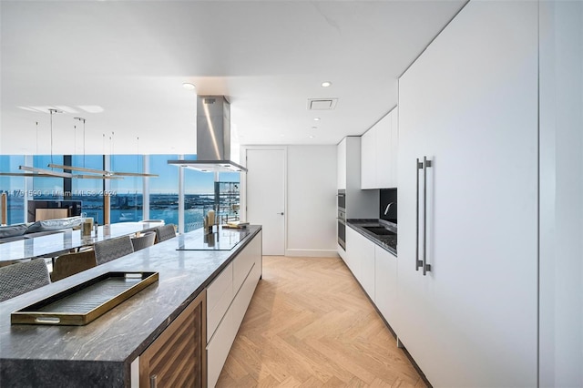 kitchen featuring island exhaust hood, light parquet flooring, white cabinets, and a spacious island