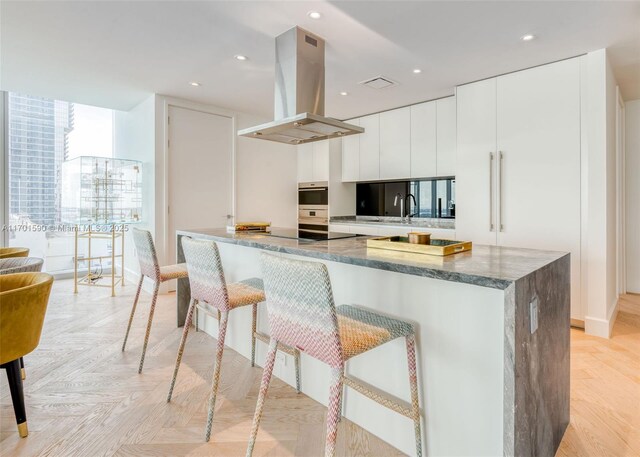 kitchen featuring white cabinets, island range hood, light parquet flooring, and oven