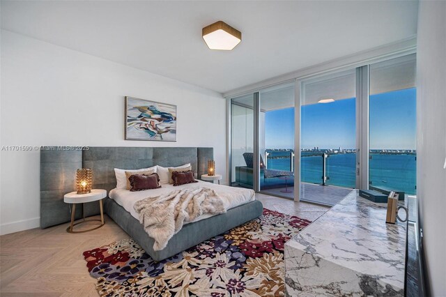 bedroom with access to exterior, a water view, a wall of windows, and hardwood / wood-style flooring