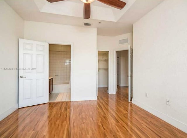 unfurnished bedroom featuring ensuite bathroom, ceiling fan, hardwood / wood-style flooring, a spacious closet, and a closet