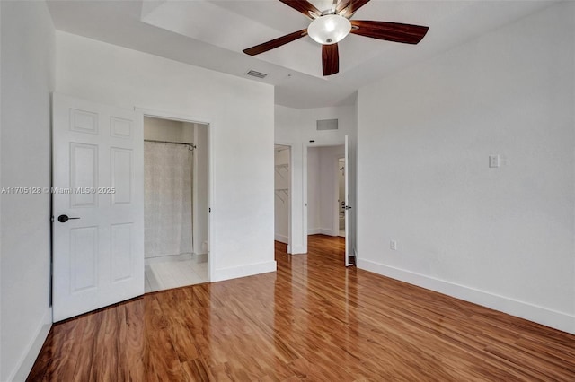 unfurnished bedroom featuring a spacious closet, wood finished floors, visible vents, and baseboards