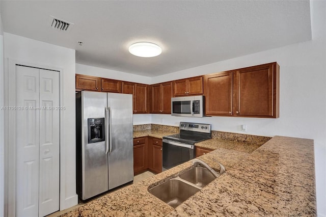 kitchen with light stone counters, brown cabinets, stainless steel appliances, visible vents, and a sink