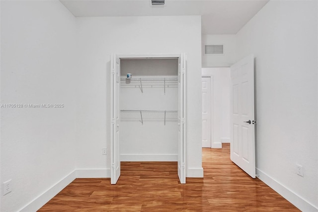 unfurnished bedroom featuring baseboards, visible vents, a closet, and wood finished floors