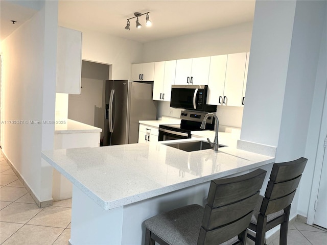 kitchen with sink, appliances with stainless steel finishes, white cabinetry, light stone countertops, and kitchen peninsula