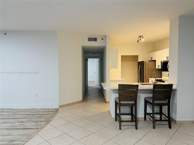 kitchen featuring light tile patterned floors, kitchen peninsula, a kitchen bar, white cabinets, and appliances with stainless steel finishes