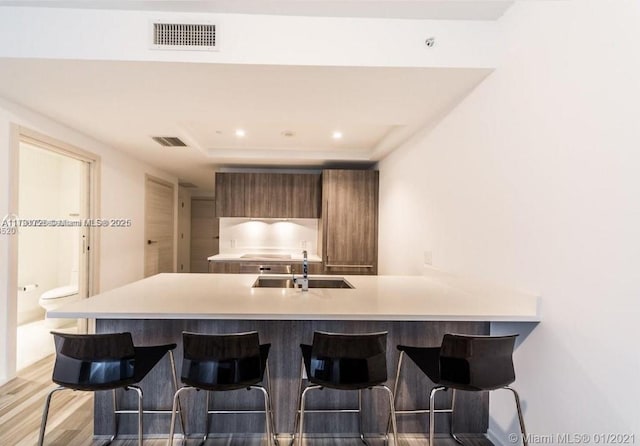 kitchen featuring a kitchen breakfast bar, kitchen peninsula, sink, and light hardwood / wood-style floors